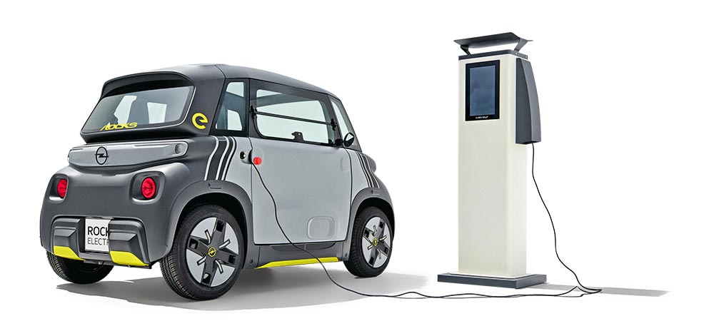 Grauer Opel Rocks-e an einer Lades&auml;ule, frontal seitlich von hinten fotografiert.