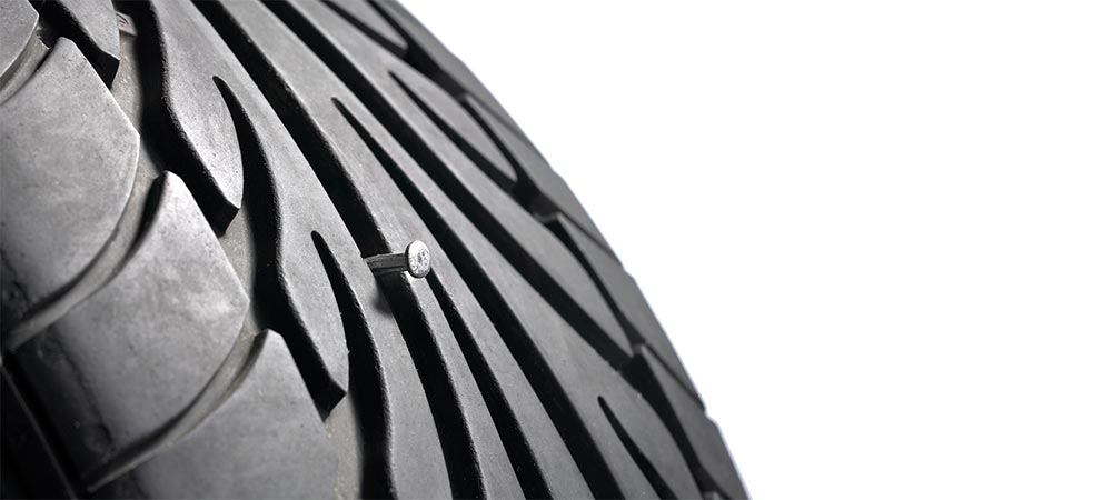 Nahaufnahme eines Autoreifens mit einem Nagel im Profil.
